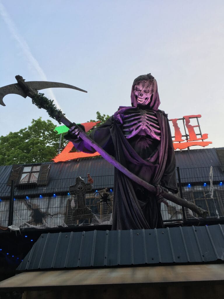 A looming, animatronic skeleton holds a scythe while grinning