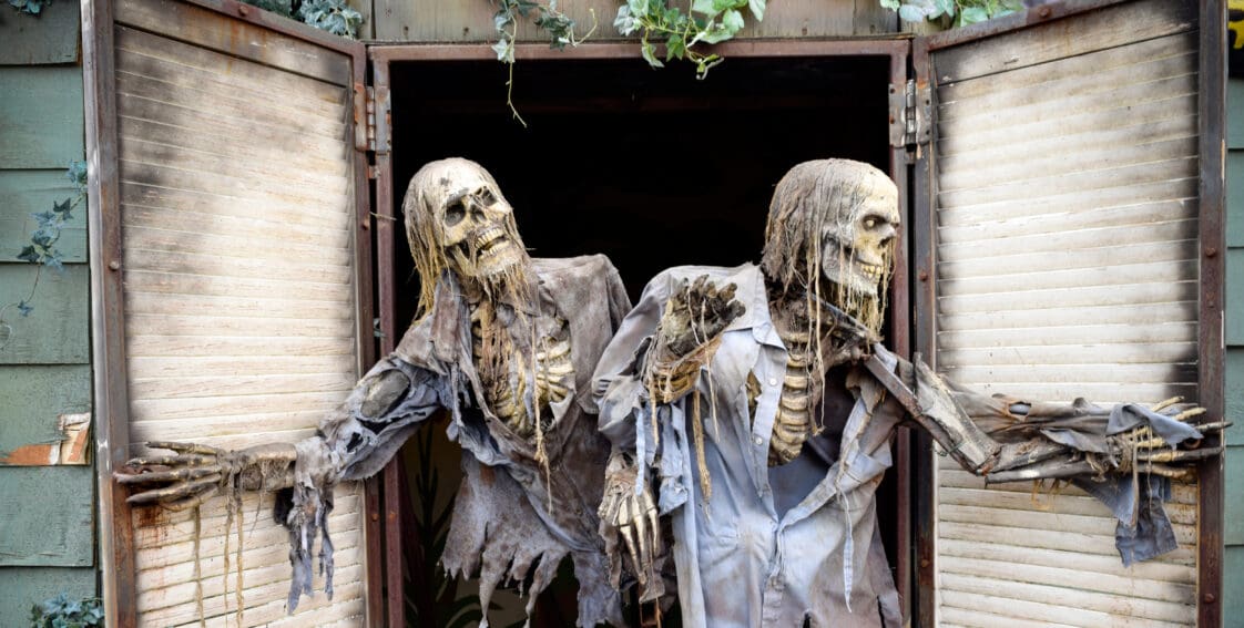 Two skeletons in ragged clothing popping out of a window of a haunted house