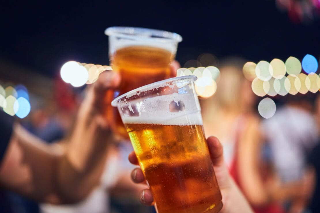 Two people hold beer in plastic cups and are clinking them together