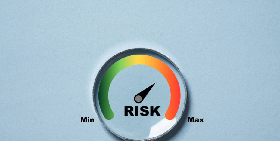 A person holds a magnifying glass. Inside the glass is a scale. The left side of the scale is green with the words 'Min' and the right side is red with the word 'Max.' At the center of the scale is the word 'Risk.'